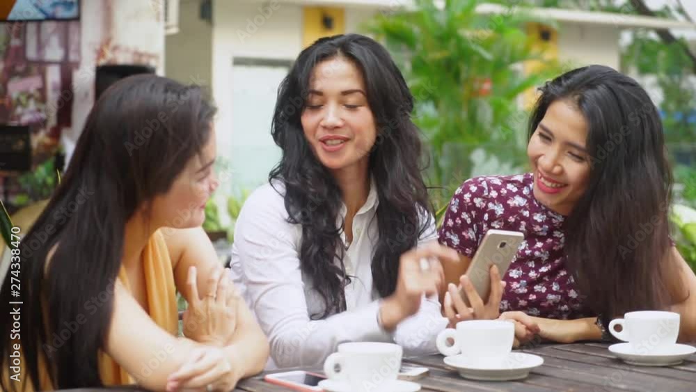 Group of cheerful young women gossiping together while using smartphone and drinking coffee in the cafe Group of cheerful young women gossiping together while using smartphone and drinking coffee in the cafe
