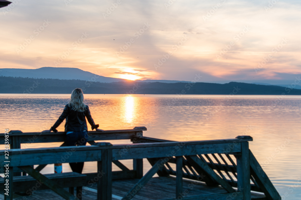 silhouette of a woman sitting on pier at sunset
