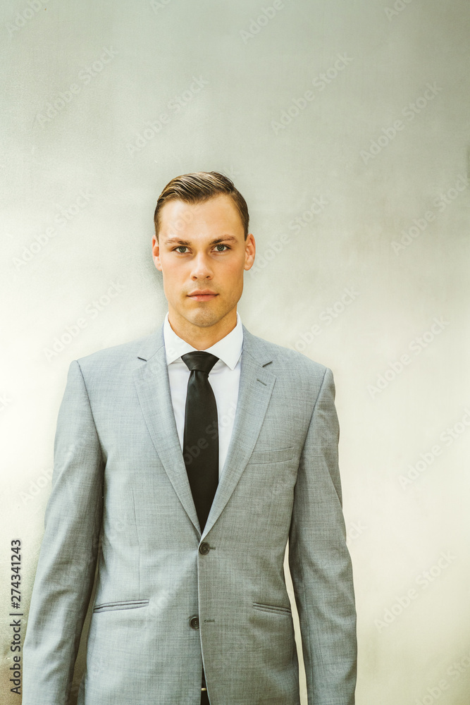 Portrait of Young European Businessman in New York City. Young Man wearing gray blazer, white shirt, black tie, standing against silver metal background, confidently looking at you.. Portrait of Young European Businessman in New York City. Young Man wearing gray blazer, white shirt, black tie, standing against silver metal background, confidently looking at you..