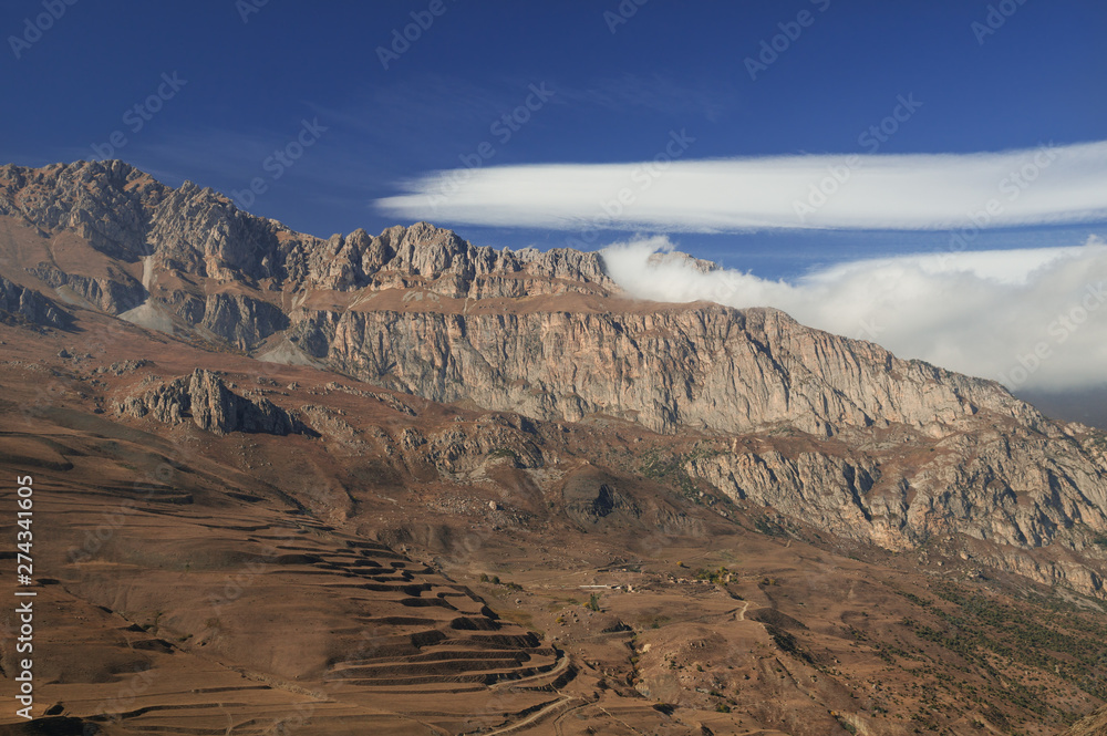 Majestic mountain view - rocky peaks with brownish withered grassy slopes under blue sky with blindingly white clouds