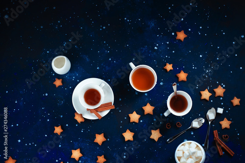 Teatime with star-shaped cookies. White porcelain cups on a starry sky background. Astronomy and constellation flat lay with copy space