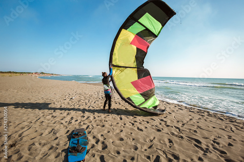 Handsome Caucasian man professional surfer standing  on the sandy beach with his kite and board.