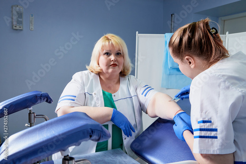 Experienced doctor fat woman and aspiring young doctor discussing the medical problems in the gynecological office