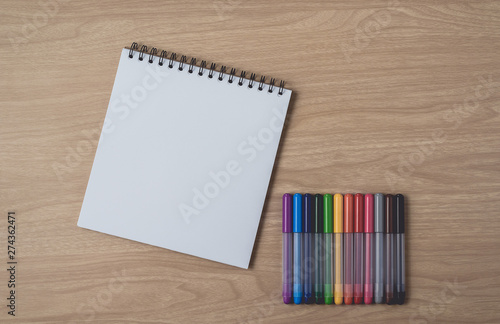 Notepad or notebook with Many colorful pens on brown wood table.using for education, business background