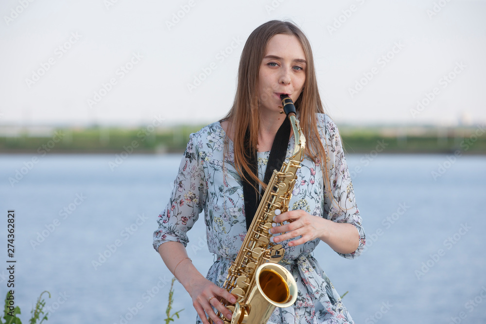 Young woman with saxophone with nature background - obrazy, fototapety, plakaty 