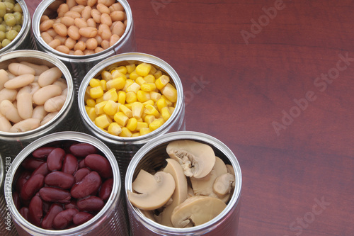 Canned green peas, beans, corn, olives and mushrooms in tin cans. Preserved food on wooden table with space for text