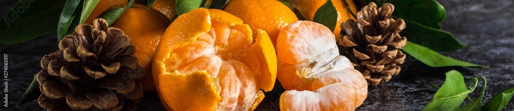 Banner of orange tangerines with green leaves on dark background. Peeled mandarin slices and cones Banner of orange tangerines with green leaves on dark background. Peeled mandarin slices and cones