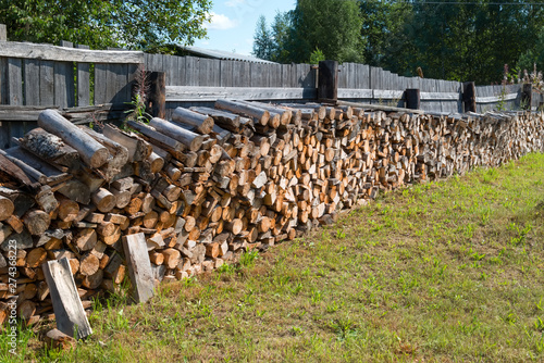 Chopped firewood stacked in a woodpile near the fence in the village
