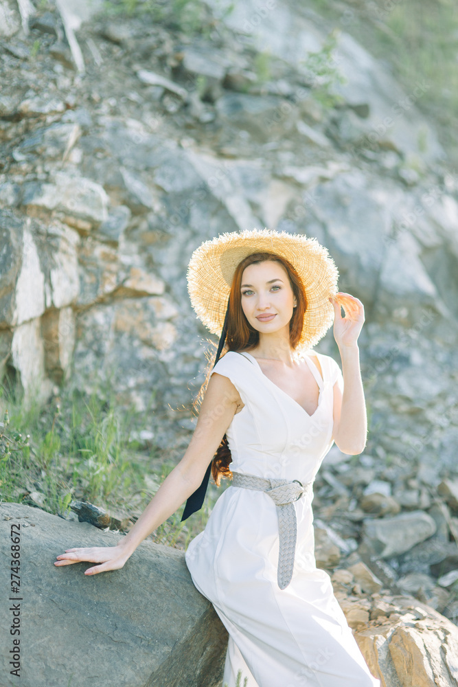 Summer photo shoot in the Park at the rocks and stones. Beautiful girl in white dress and hat.