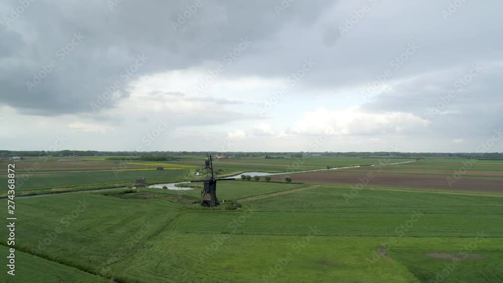 AERIAL view of open green fields with Dutch windmills overlooking the cloudy skyline. AERIAL view of open green fields with Dutch windmills overlooking the cloudy skyline.