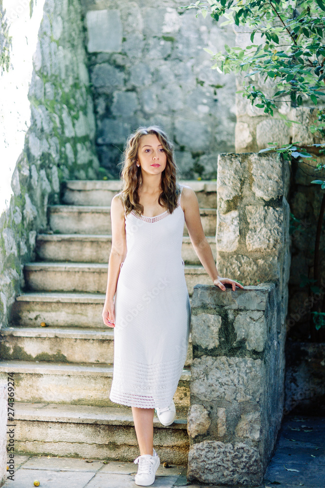 Summer photo shoot on the streets of Kotor, Montenegro. Beautiful girl in white dress and hat.