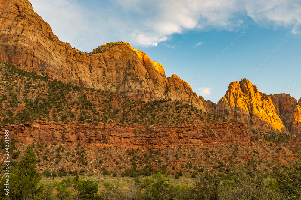 A landscape view of the amazing rugged landscape from the canyon floor at Zion National Park, USA against a beautiful bright blue sky and moon in the distance