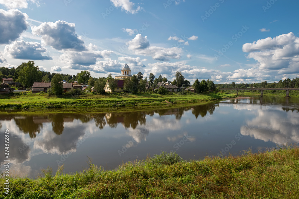 View of the left bank of the river Msta and the Church of the Assumption of the Blessed Virgin Mary on a summer day View of the left bank of the river Msta and the Church of the Assumption of the Blessed Virgin Mary on a summer day