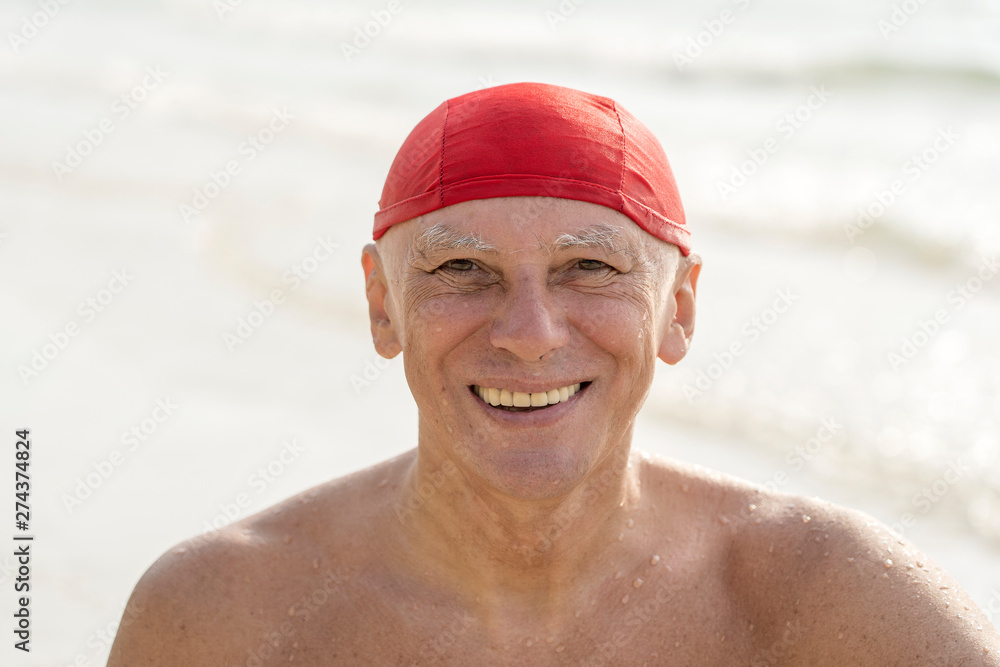 Elderly man in a red swimming hat on the beach near the sea water