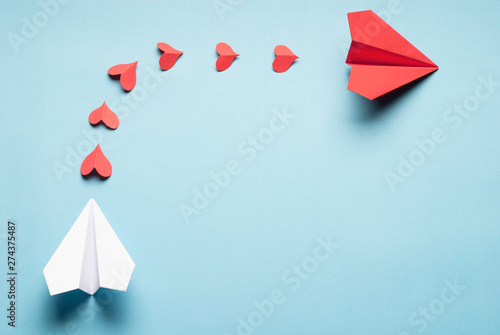 Red and white origami planes connected with red paper hearts. Love concept.