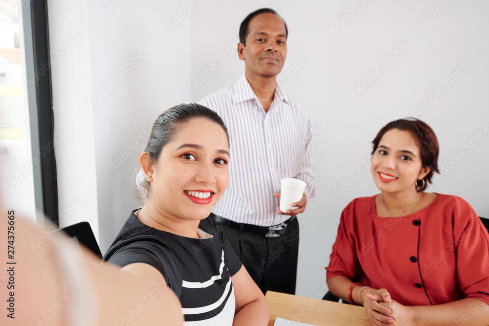 Group of business people sitting at the table and posing at camera they making selfie portrait on mobile phone at office Group of business people sitting at the table and posing at camera they making selfie portrait on mobile phone at office