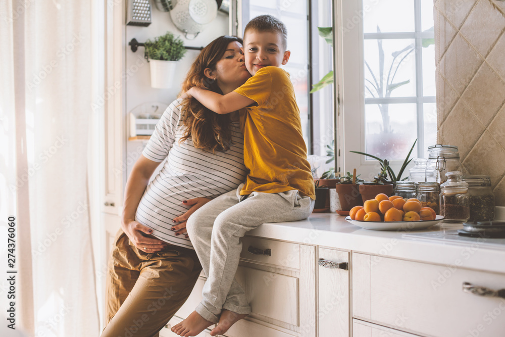 Pregnant mom with kid playing together in the kitchen Pregnant mom with kid playing together in the kitchen