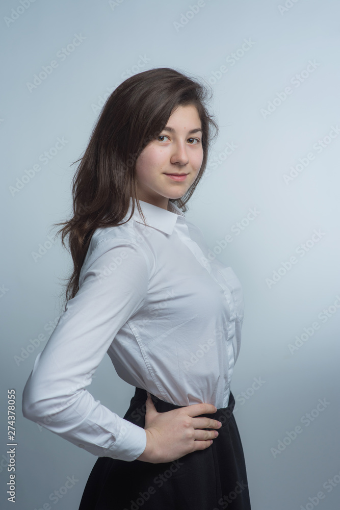 Portrait of a young beautiful brunette with lush curly hair in a white shirt and gray skirt Portrait of a young beautiful brunette with lush curly hair in a white shirt and gray skirt