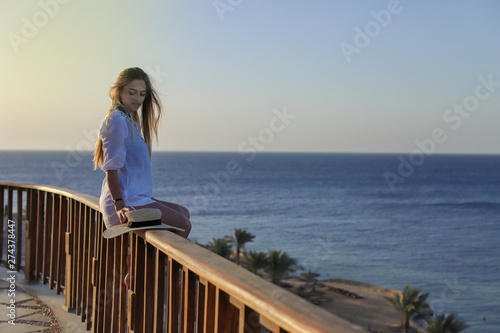 Portrait of a Sexy beautiful tanned woman relaxing in swimsuit and with light beach dress on terrace with blue sea and sky on background. Summer Vacation Concept. © Mike Sagan