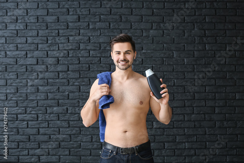Handsome man with bottle of shampoo and towel on dark background