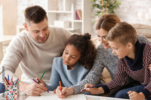 Happy couple with little adopted children drawing at home photo