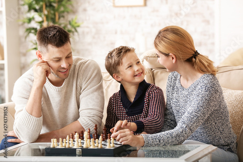 Happy couple with little adopted children playing chess at home