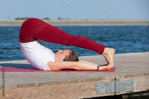 Young girl practices yoga on the shore of the lake, the concept of enjoying privacy and concentration, sunlight