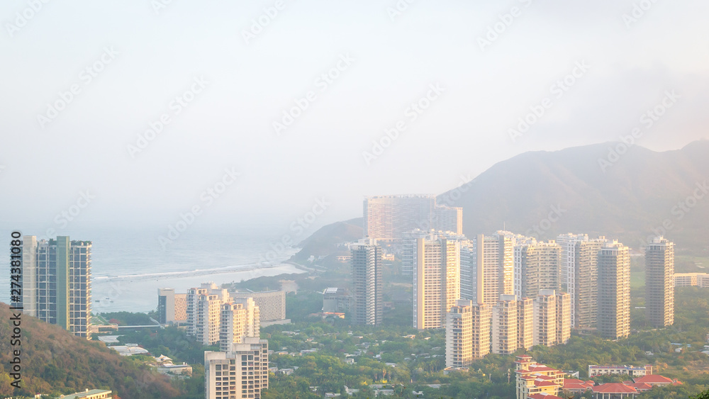 Naklejka premium View of one of the districts of Sanya city. Visible are the skyscrapers. Sunset, blur, haze. Hainan Island, China.