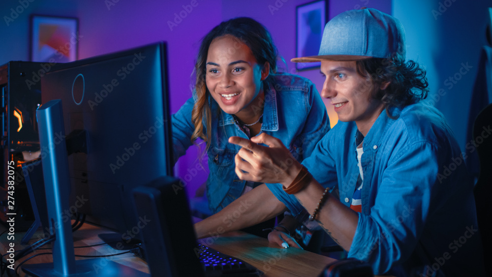 Pretty Black Girl Actively Talks and Explains Something to Her Friend and Points on a Computer Screen. They Have a Discussion about New Creative Ideas. Cozy Room is Lit with Warm and Neon Light.