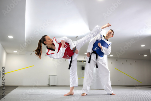 Fototapeta Young woman training martial art of taekwondo with her coach