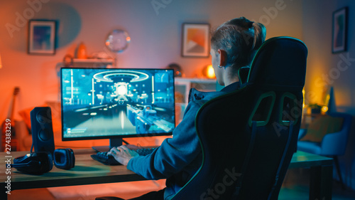 Back Shot of a Gamer Playing First-Person Shooter Online Video Game on His Powerful Personal Computer. Room and PC have Colorful Neon Led Lights. Cozy Evening at Home.