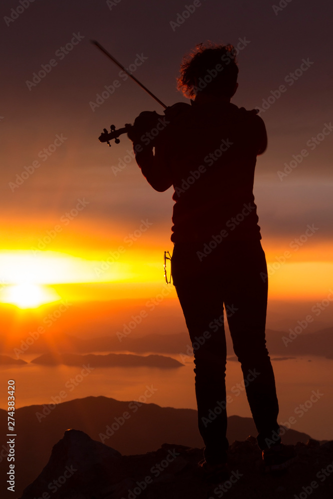 Silhouette of a woman with a violin at sunset on top of the mountain