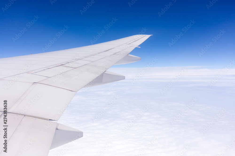 Wing of airplane flying above the clouds in the sky background.