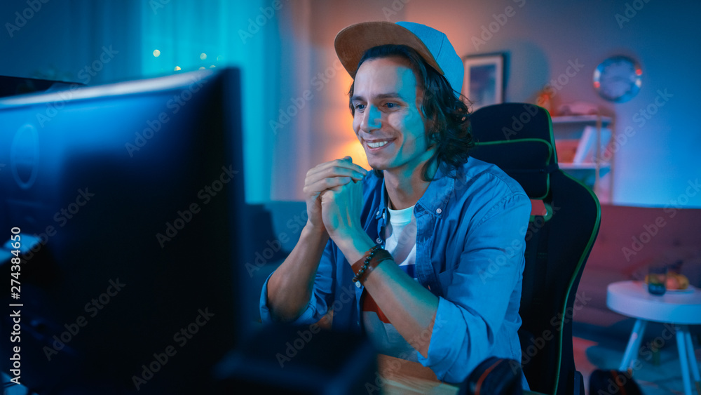 Handsome Excited Young Man Watching an Action Video on a Computer. He is Happy. Cozy Room is Lit with Warm Light. Handsome Excited Young Man Watching an Action Video on a Computer. He is Happy. Cozy Room is Lit with Warm Light.