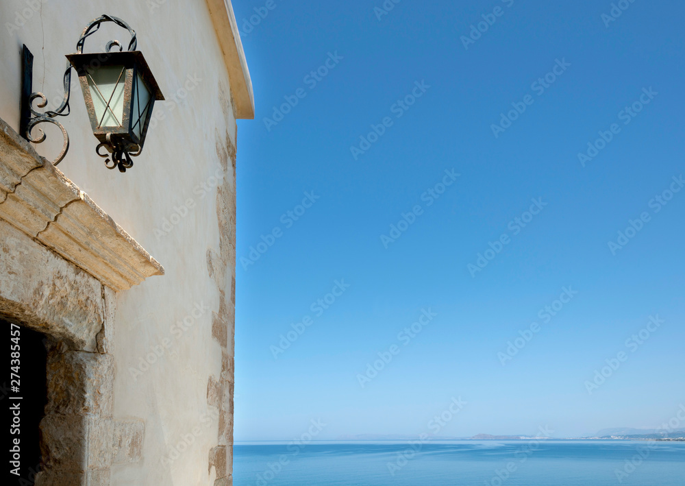 Sommermotiv am Mittelmeer, Wand mit Laterne vor blauem Himmel und blauem Wasser