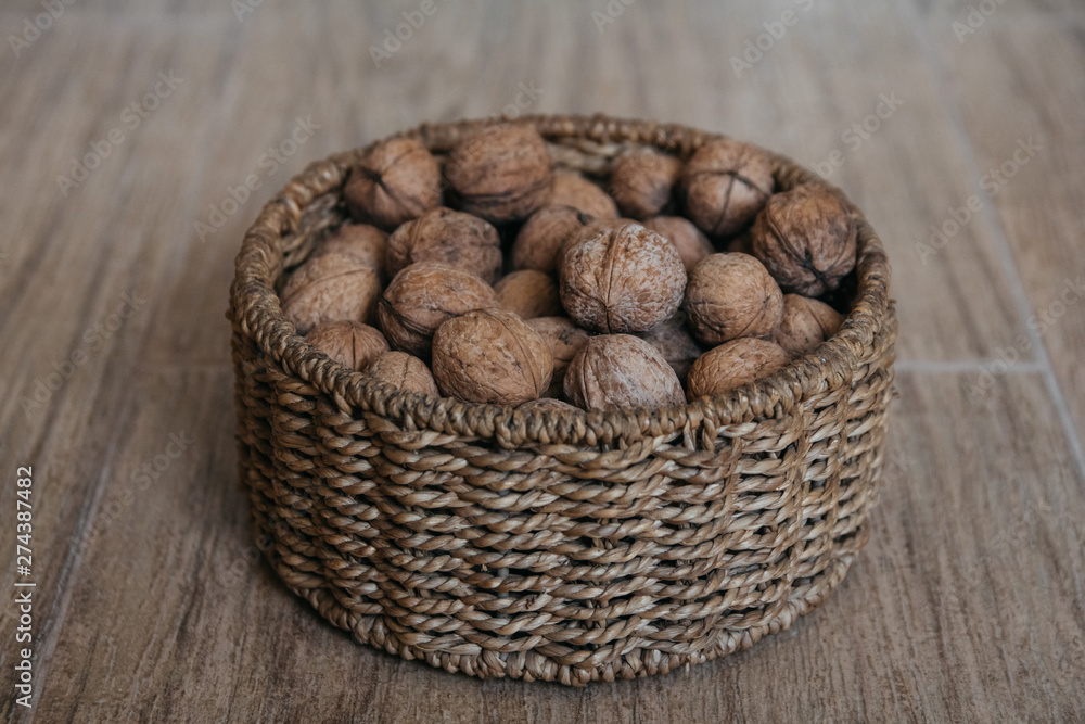 Walnuts in a round wicker basket on a wooden background. Central composition.