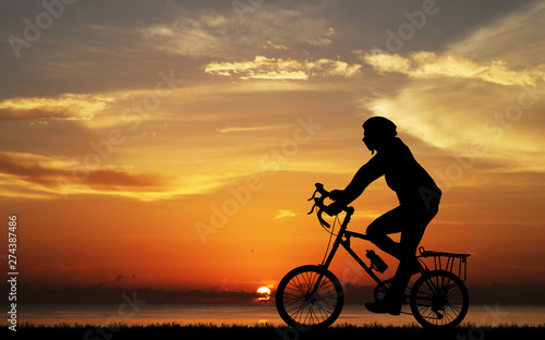 Silhouette man and bike relaxing on blurry sunrise sky background.