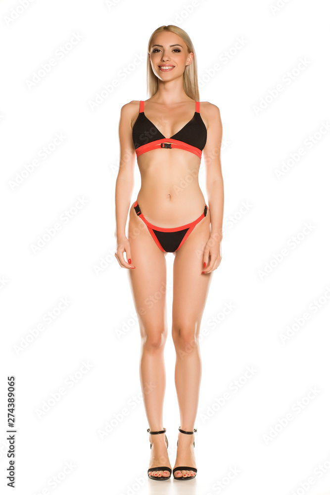 Pretty young lady in black bikini swimsuit and sandals on white background