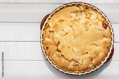 Apple pie with crispy crust in round baking dish on white wooden table, top view with copy space