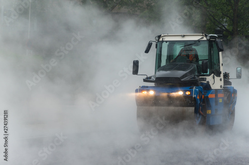 Asphalt drum roller at work during rain causing heavy steam