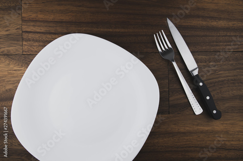 Empty white plate  spoon and knife isolated on wooden background. diet concept.