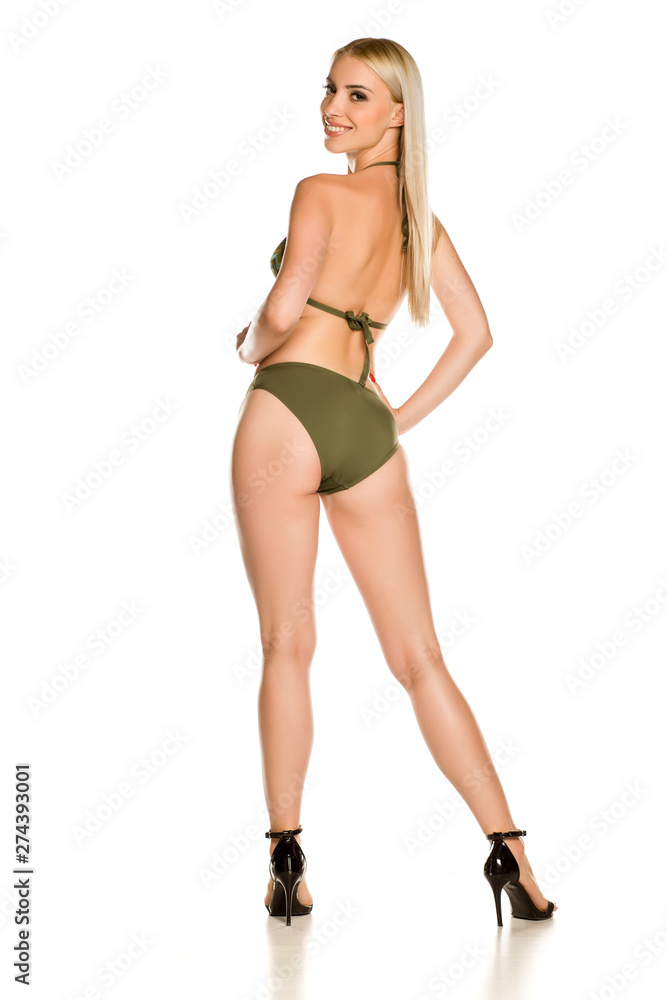 Back view of pretty young smiling lady in green bikini swimsuit and sandals on white background