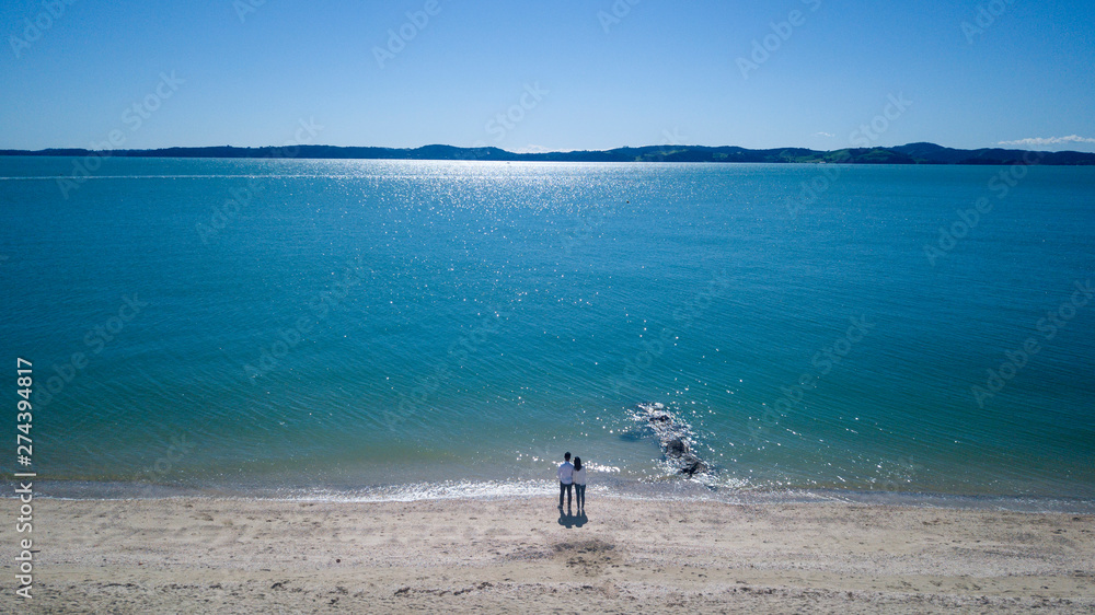 aerial shot of couple looking out to the ocean on the beach with clear water on a bright sunny day aerial shot of couple looking out to the ocean on the beach with clear water on a bright sunny day