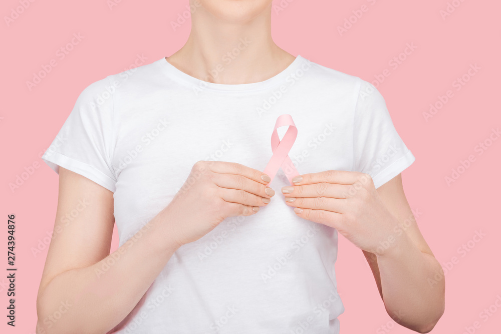 partial view of woman in white t-shirt holding pink breast cancer sign isolated on pink partial view of woman in white t-shirt holding pink breast cancer sign isolated on pink