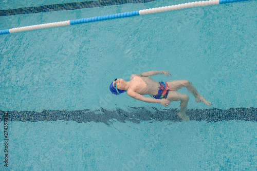 top view of a 7-year boy swimming backstroke in a swimming pool