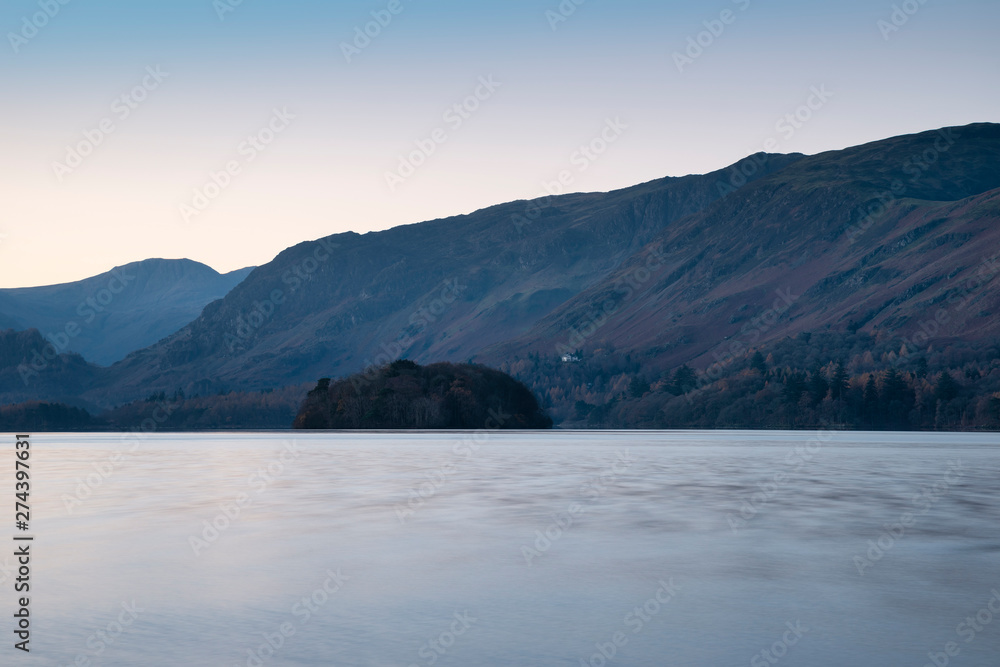 Stunning long exposure landscape image of Derwent Water in Lake District during Autumn Fall sunrise with soft pastel colors