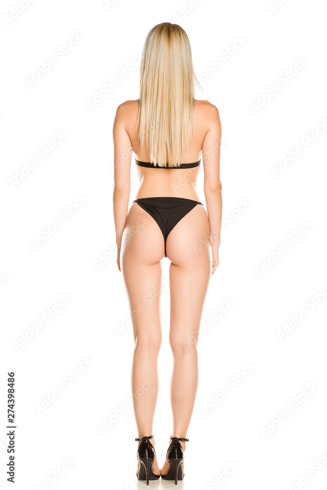 Back view of pretty young lady in black swimsuit and sandals on white background
