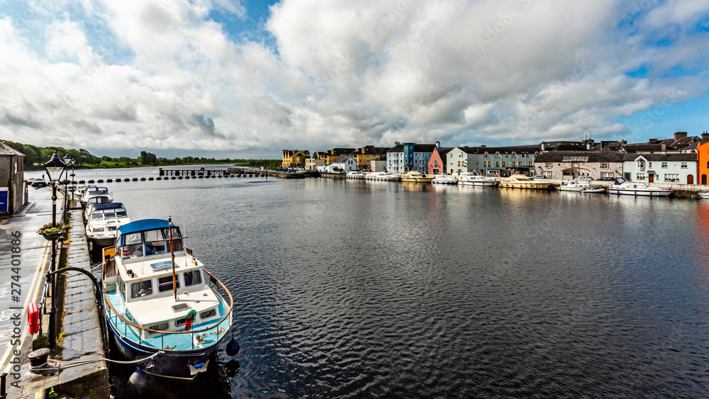 Fototapeta premium Shannon river with boats anchored at docks, cityscape with quaint houses in Athlone town in the background, cloudy day with cloudy blue sky in County Westmeath, Ireland