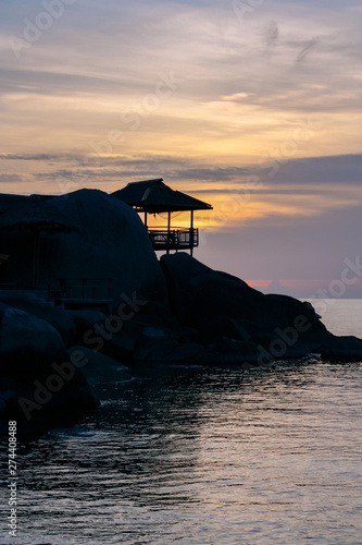 Beautiful sunset on the paradise island of Thailand. Tropical bungalow on a mountain with stones against the background of the sea and the sun