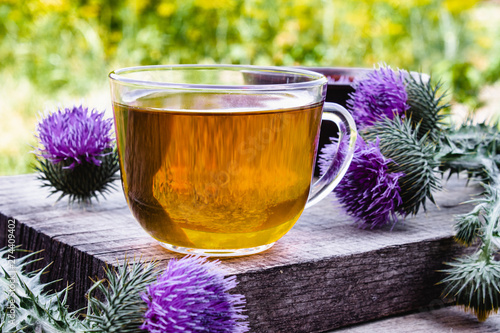 A cup of thistle tea on a woody background on nature. Thistle flowers near the cup with tea. Herbal tea.